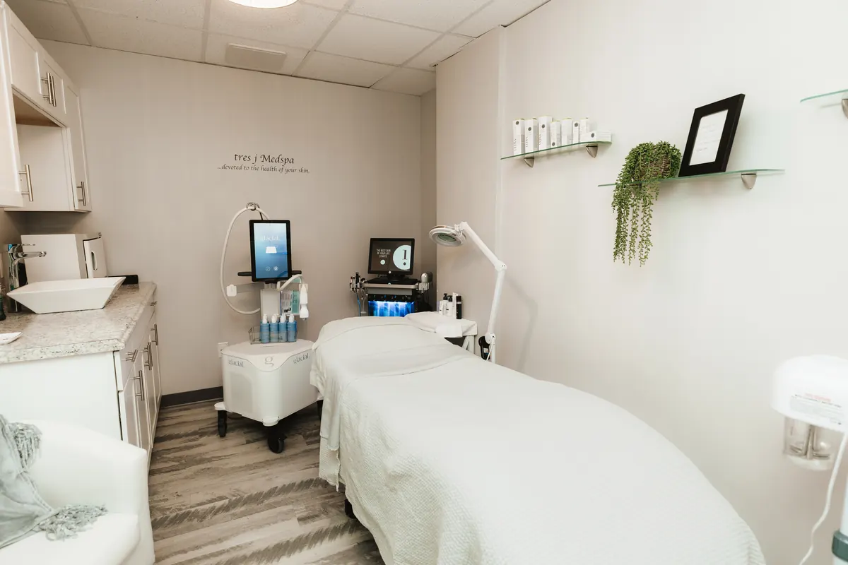 Treatment bed with devices beside shelves, under tres j Medspa wall lettering