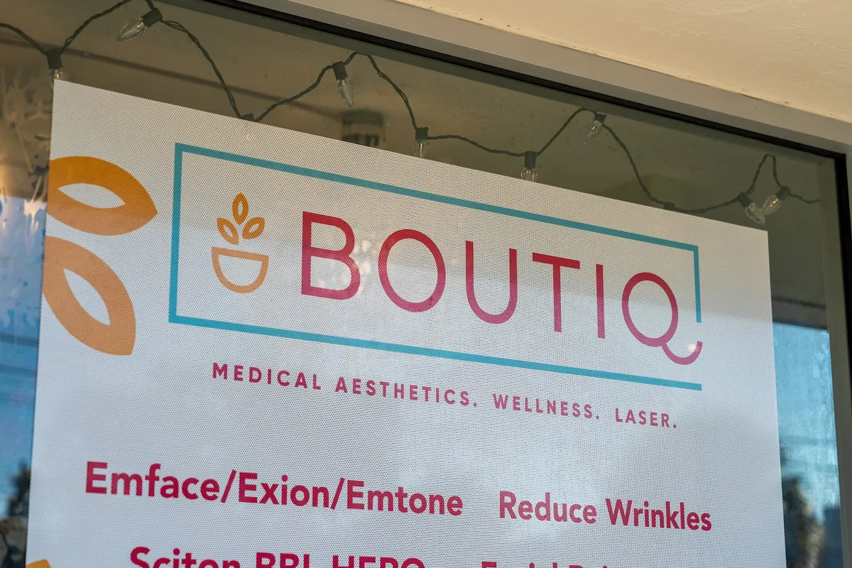 Boutiq Medical Aesthetics, Wellness, Laser sign in a storefront window beneath string lights