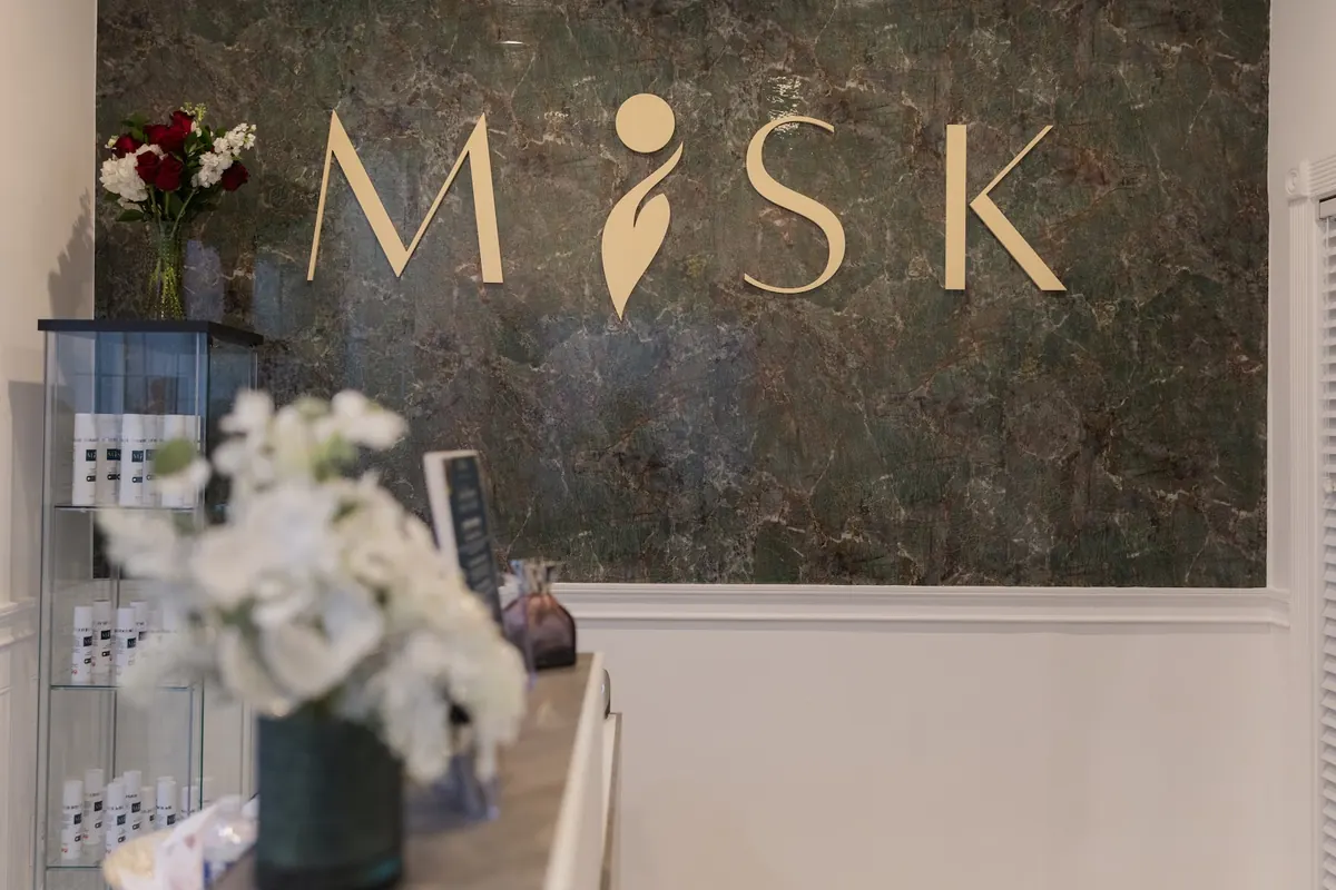 Gold MISK lettering on a green marble wall behind a reception counter with white flowers