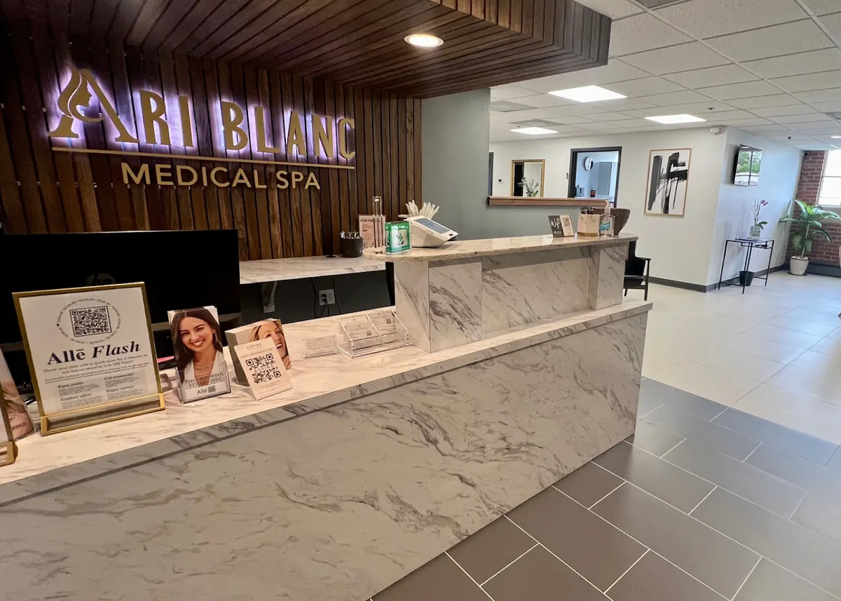 Marble reception counter beneath a lit gold Ari Blanc Medical Spa sign on a wood slat wall
