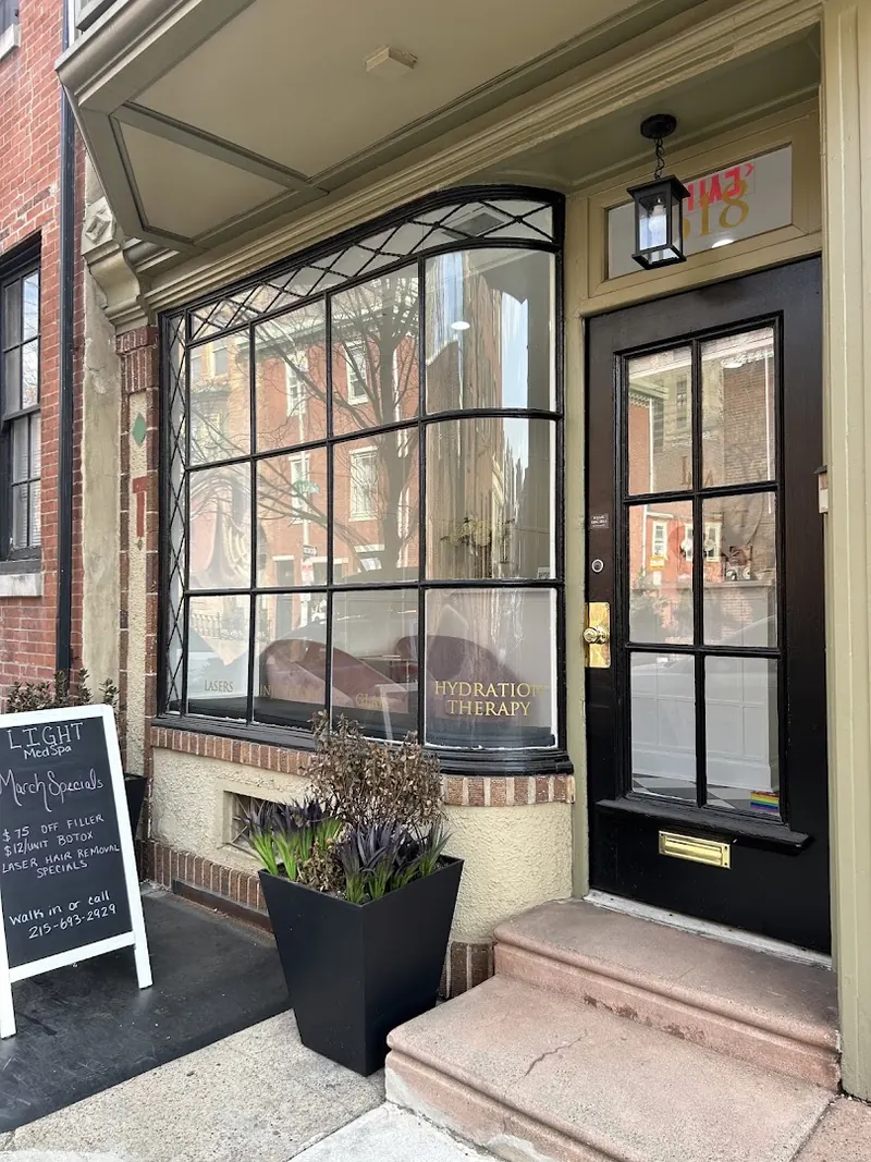 Brick rowhouse storefront with black door, bay window and a chalkboard sign reading Light MedSpa