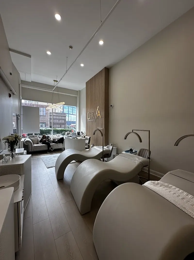 Long treatment room with curved white loungers and a DAYA logo on a wood slat wall