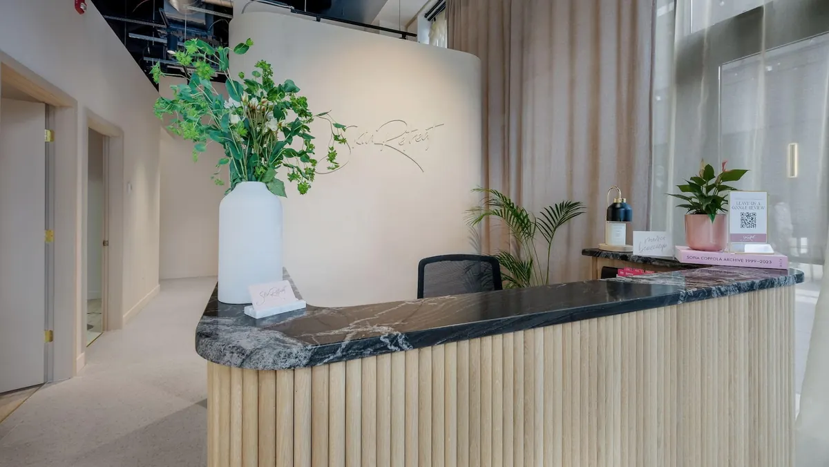 Marble-topped fluted wood reception desk before a curved wall with a Skin Retreat script sign