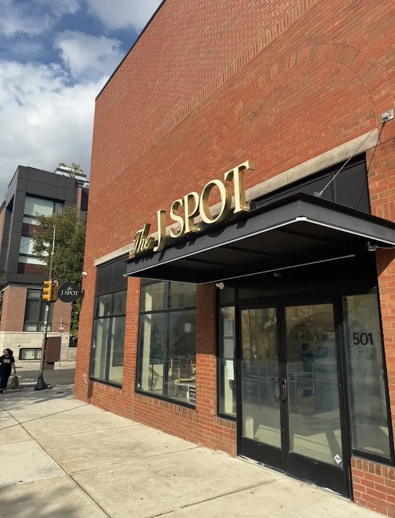 Brick corner building with gold The J Spot sign above a black awning and glass doors