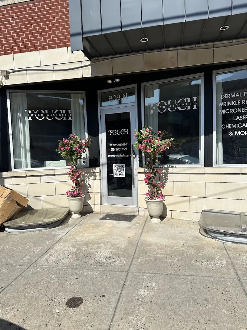 Storefront with TOUCH AESTHETIC window lettering, 808 N above the door and flowering topiaries