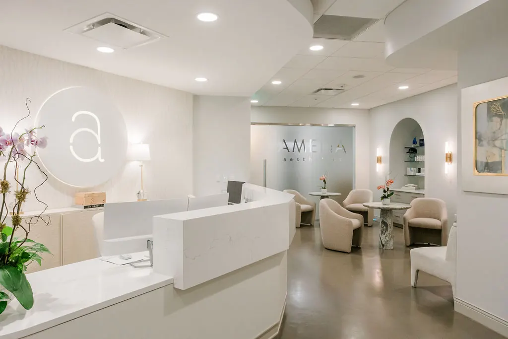 Curved white reception desk with a round lit 'a' logo and a seating area beyond frosted glass lettering