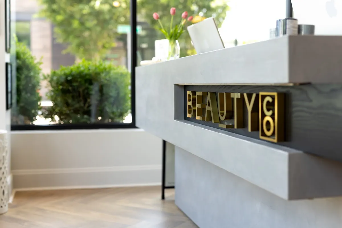 Grey reception desk with gold BEAUTY CO lettering beside a street-facing window