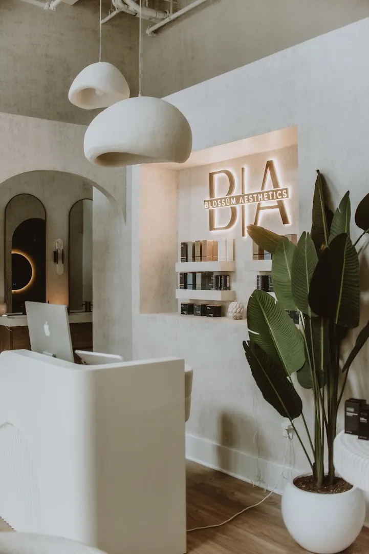 Reception desk beside a backlit Blossüm Aesthetics wall sign above skincare shelves