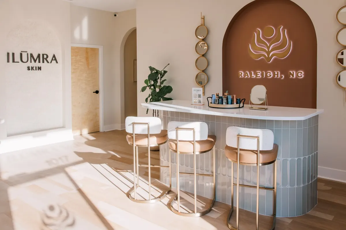 Tiled reception bar with three stools beside ILŪMRA Skin and Raleigh, NC wall signs
