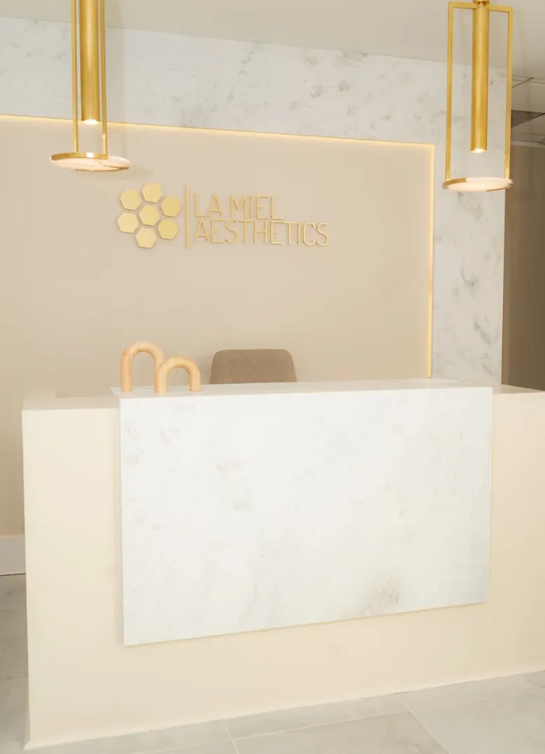 Reception desk with a marble front beneath a gold honeycomb logo and La Miel Aesthetics lettering