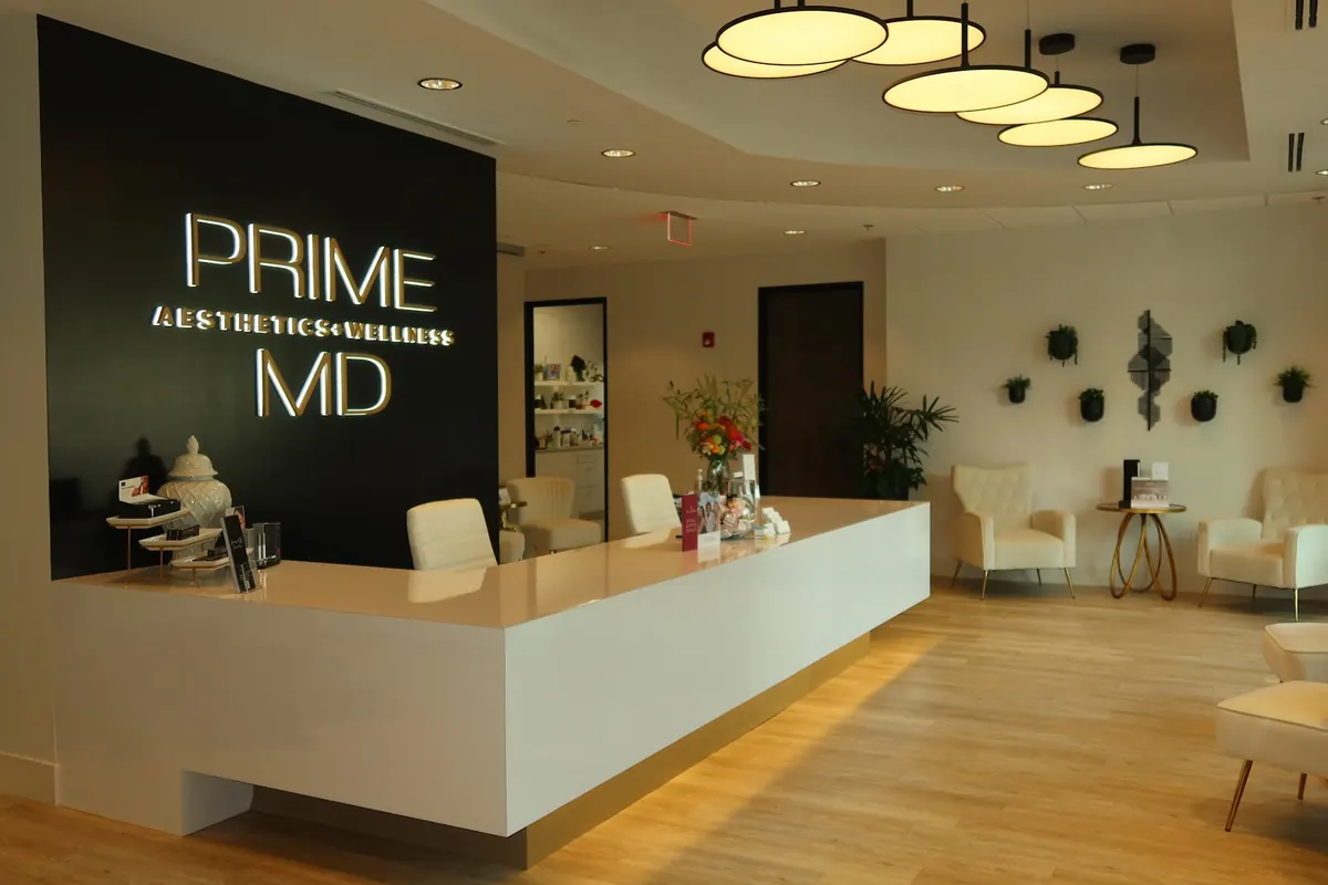 White reception desk and cream lounge chairs below a lit Prime MD Aesthetics + Wellness sign