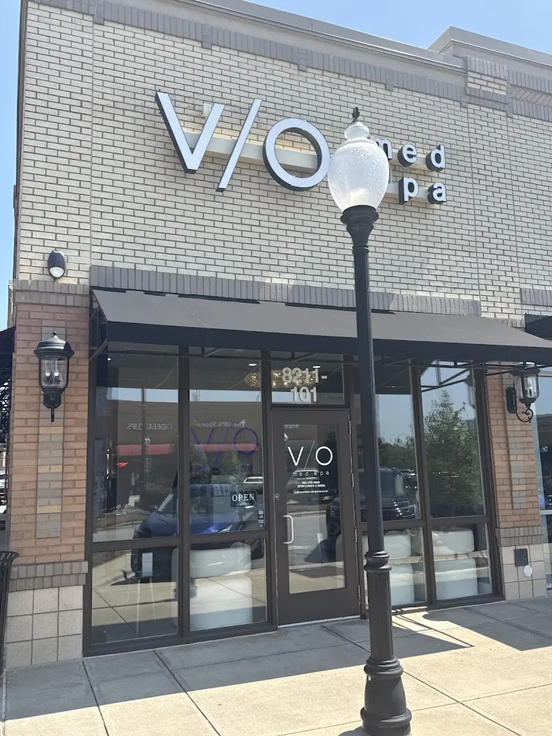 Brick storefront with V/O med spa lettering above a glass door and black awning, a lamp post in front