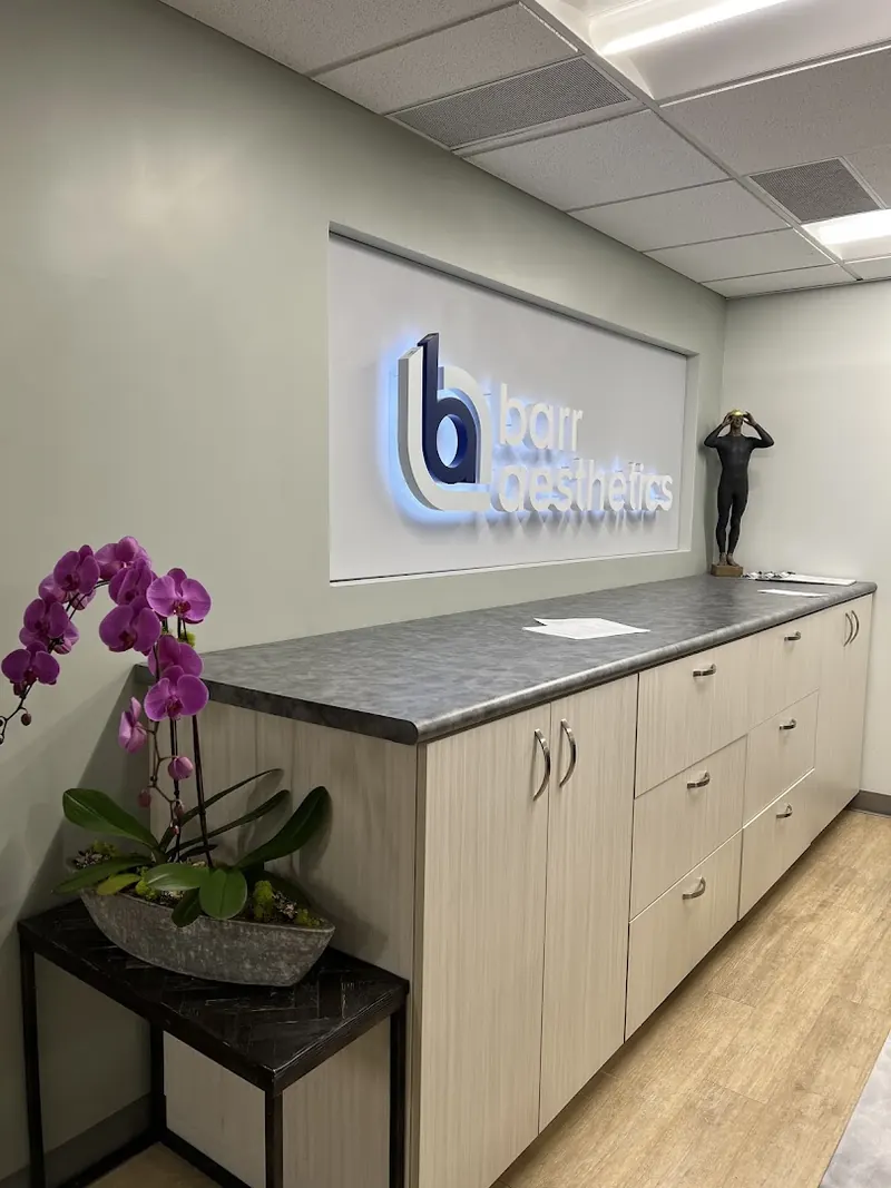 Backlit Barr Aesthetics wall sign above a long cabinet counter with a potted orchid