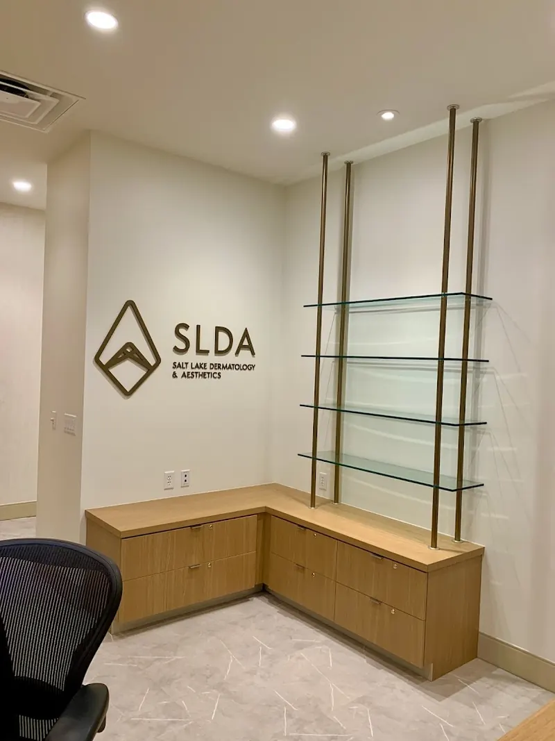 SLDA Salt Lake Dermatology and Aesthetics wall logo beside glass shelves on a wood cabinet
