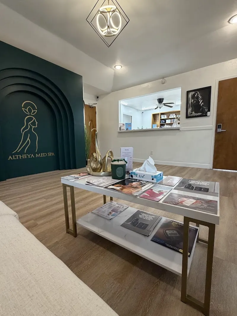 Waiting area with a low marble table beneath a green arched wall bearing the Altheya Med Spa logo