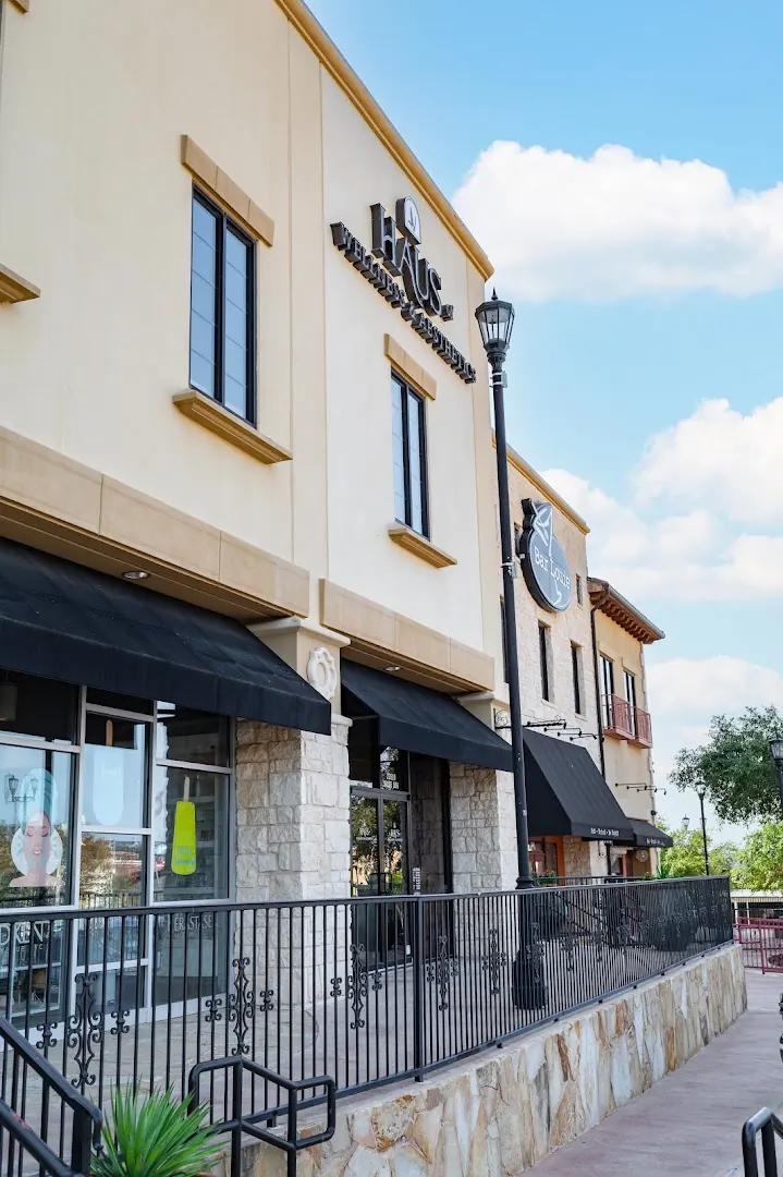 Cream stucco building with a Haus Wellness & Aesthetics sign above black canvas awnings