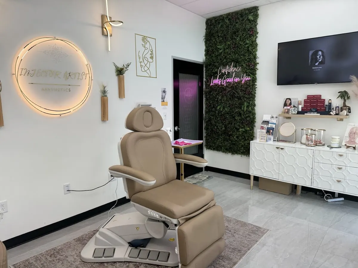 Tan treatment chair beside a backlit Injector Artist Aesthetics wall sign and green plant wall