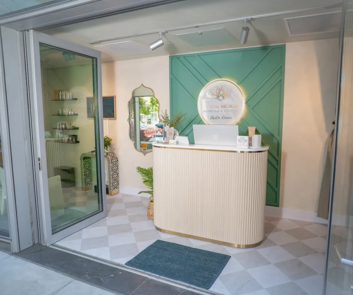 Open glass storefront door leading to a curved reception desk beneath a lit lotus-logo sign