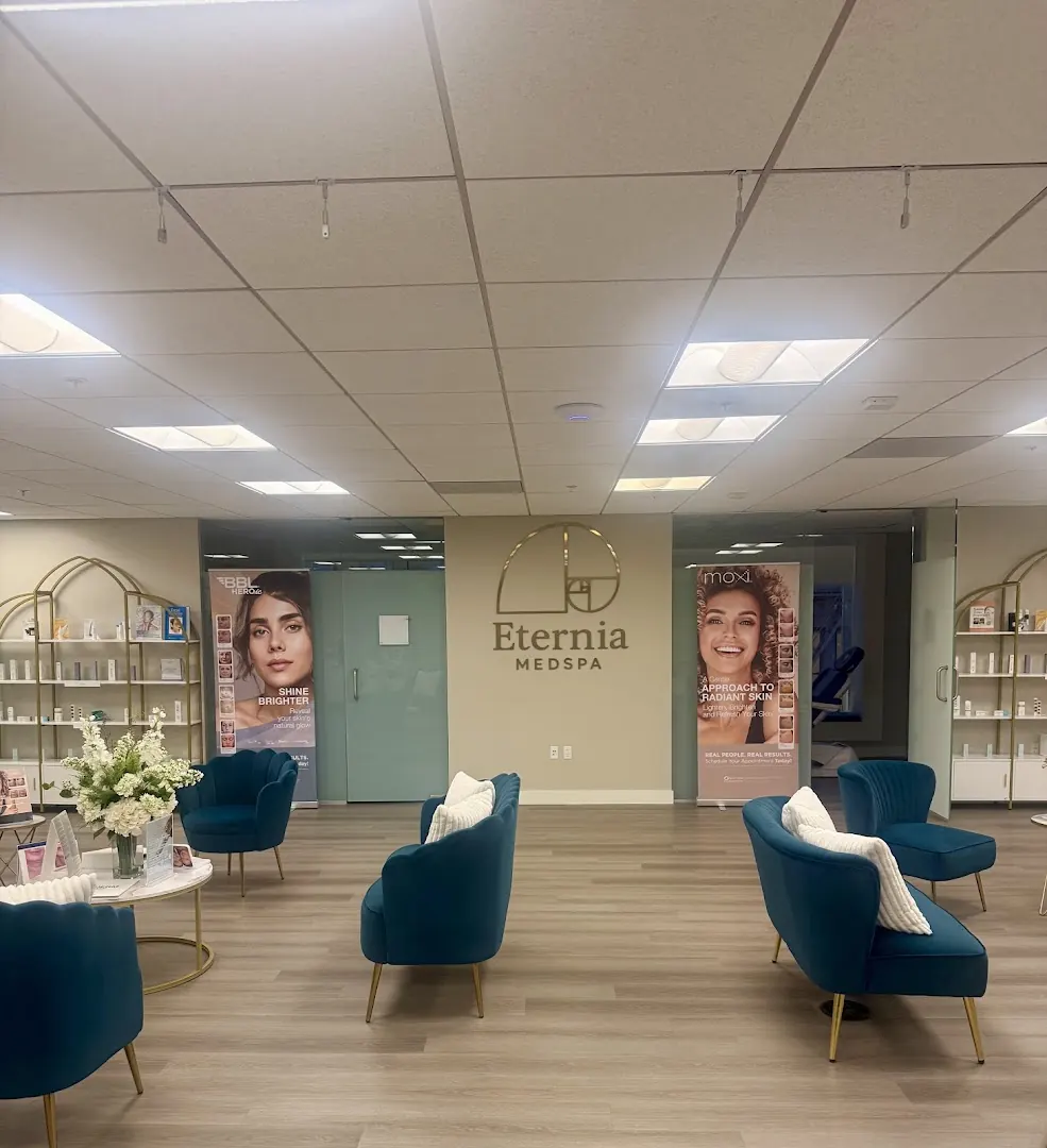 Waiting area with teal velvet chairs under a gold Eternia Medspa wall logo