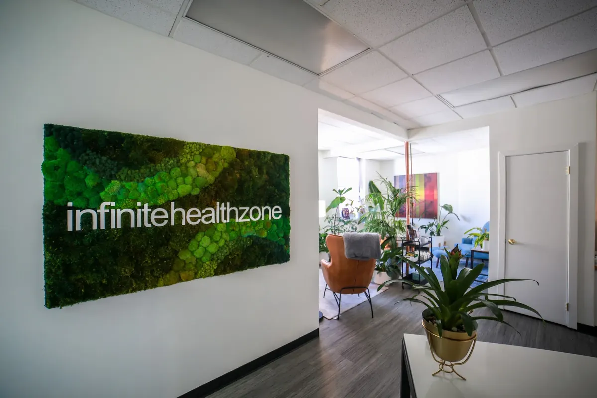 Moss wall panel with white infinite healthzone lettering beside an entry to a plant-filled lounge