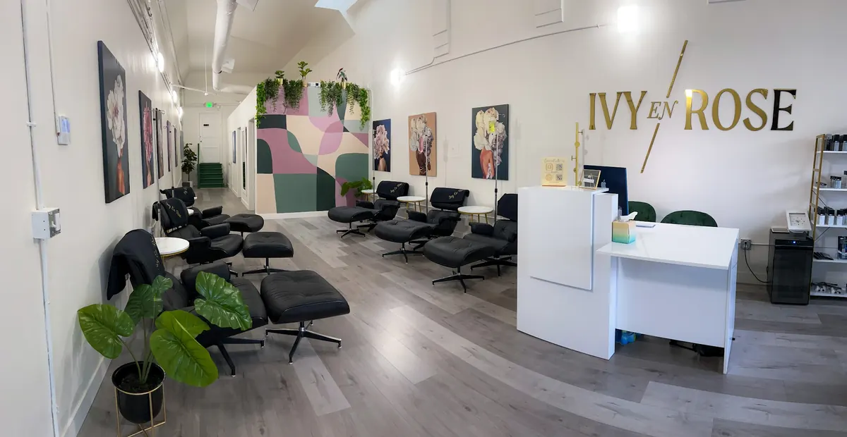 White reception desk and black recliners beneath a gold Ivy En Rose wall sign