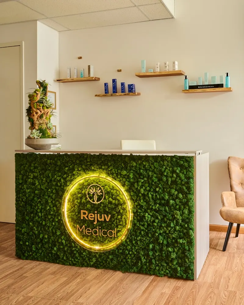 Moss-covered reception desk with a lit Rejuv Medical logo ring below product shelves