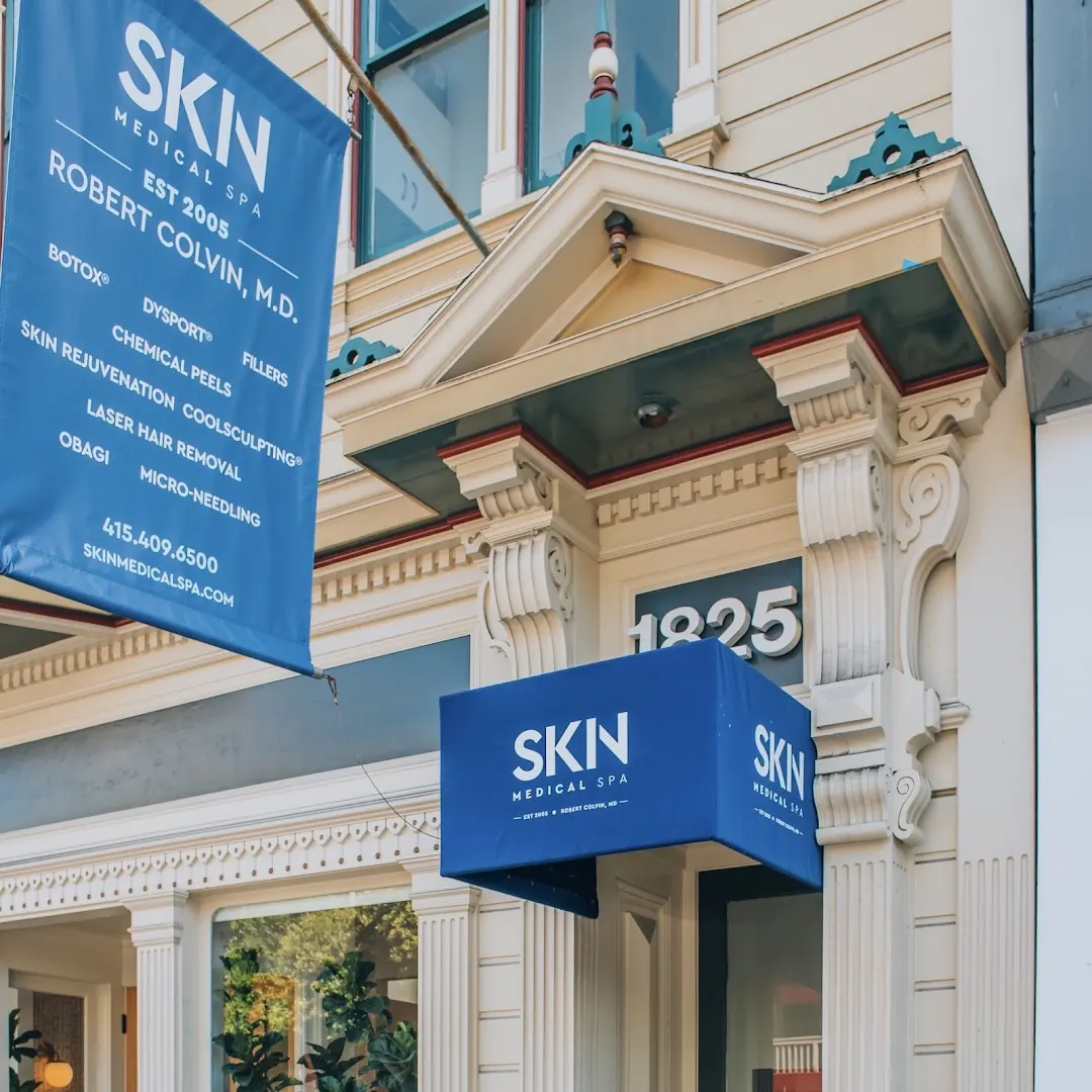 Blue SKN Medical Spa banner and awning beneath the 1825 address on a Victorian facade