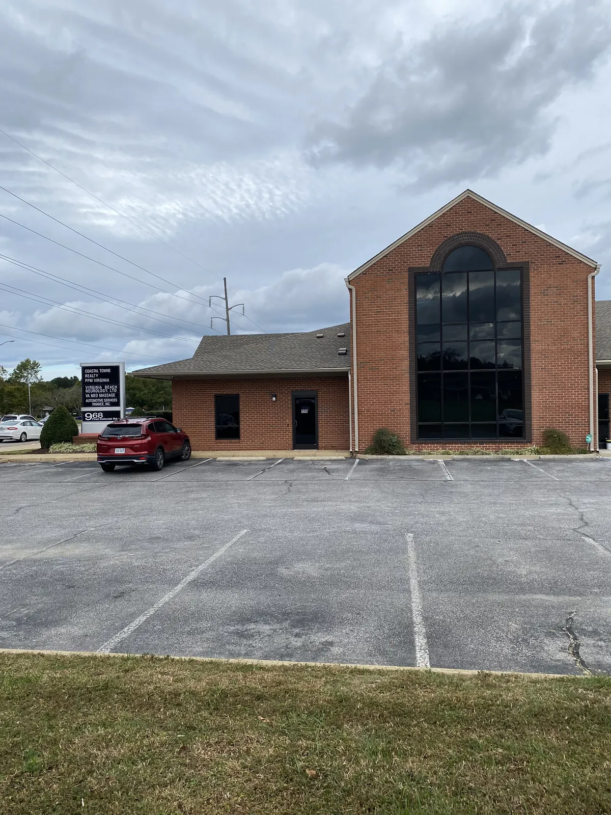 Red brick office building with a tall arched window, parking lot and a tenant sign at left