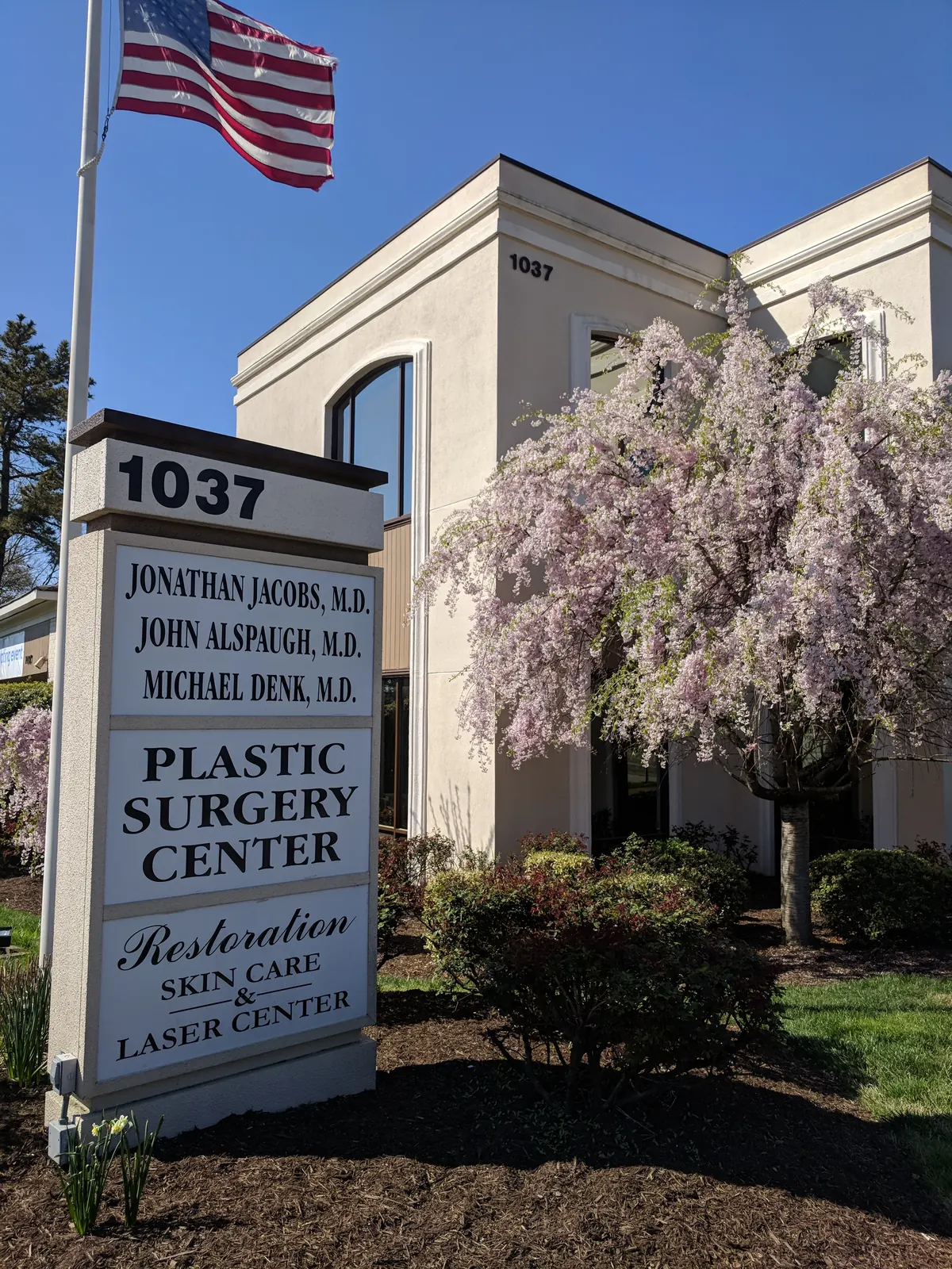 Monument sign reading 1037 Plastic Surgery Center and Restoration Skin Care and Laser Center beside a flagpole
