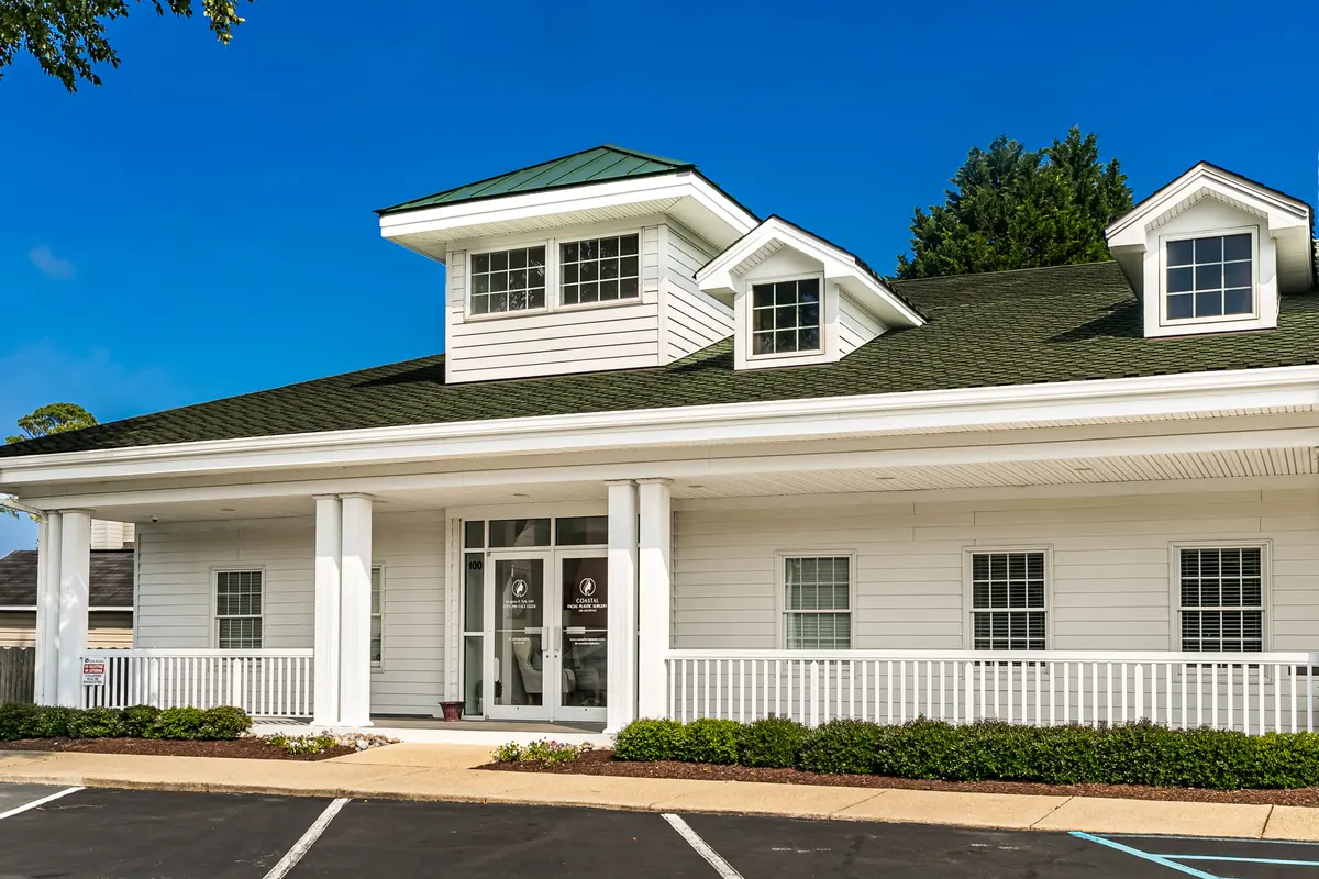 White building with a covered porch and dormers; glass double doors carry a practice decal