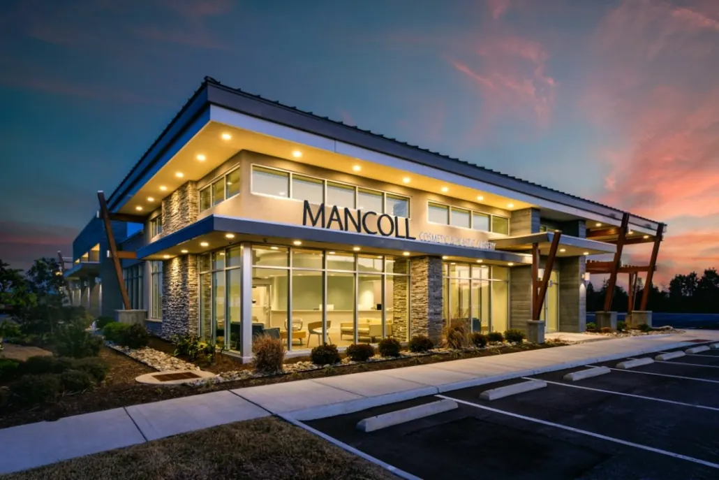 Two-story medical office building with MANCOLL lettering above the glass entrance at dusk