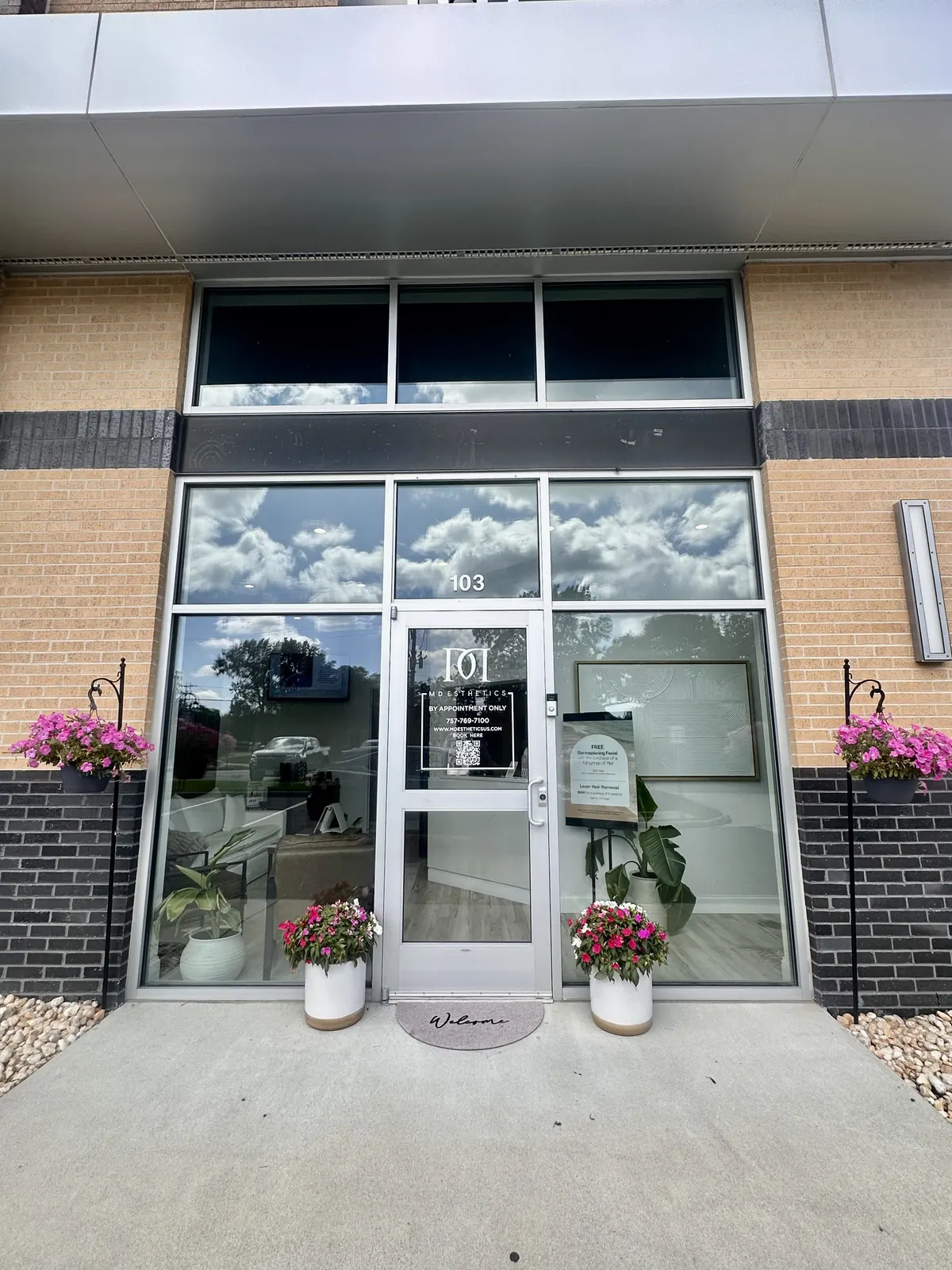 Glass entrance door with logo decal, planters and a welcome mat under the number 103