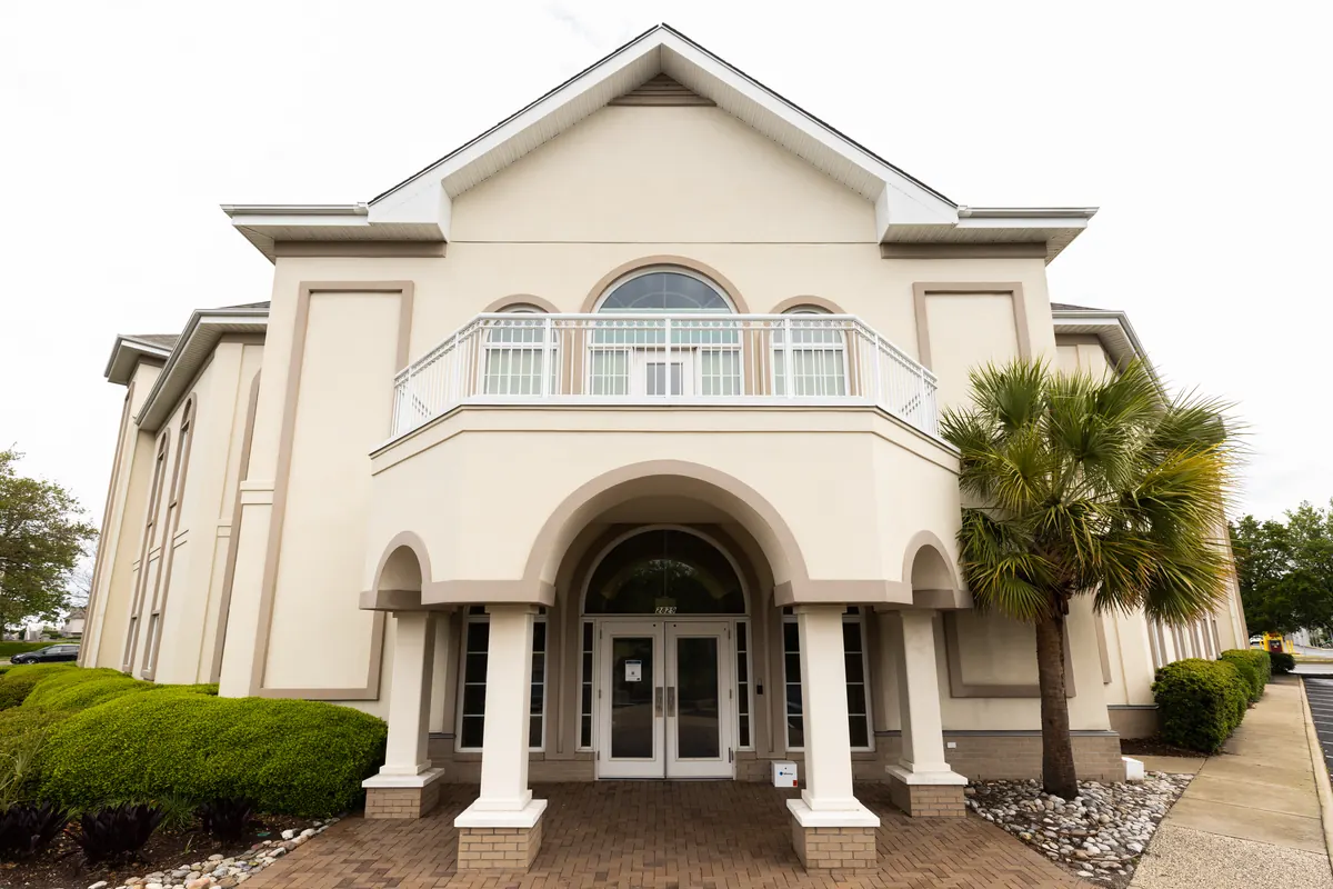 Cream stucco office building with an arched entrance portico, balcony and palm tree