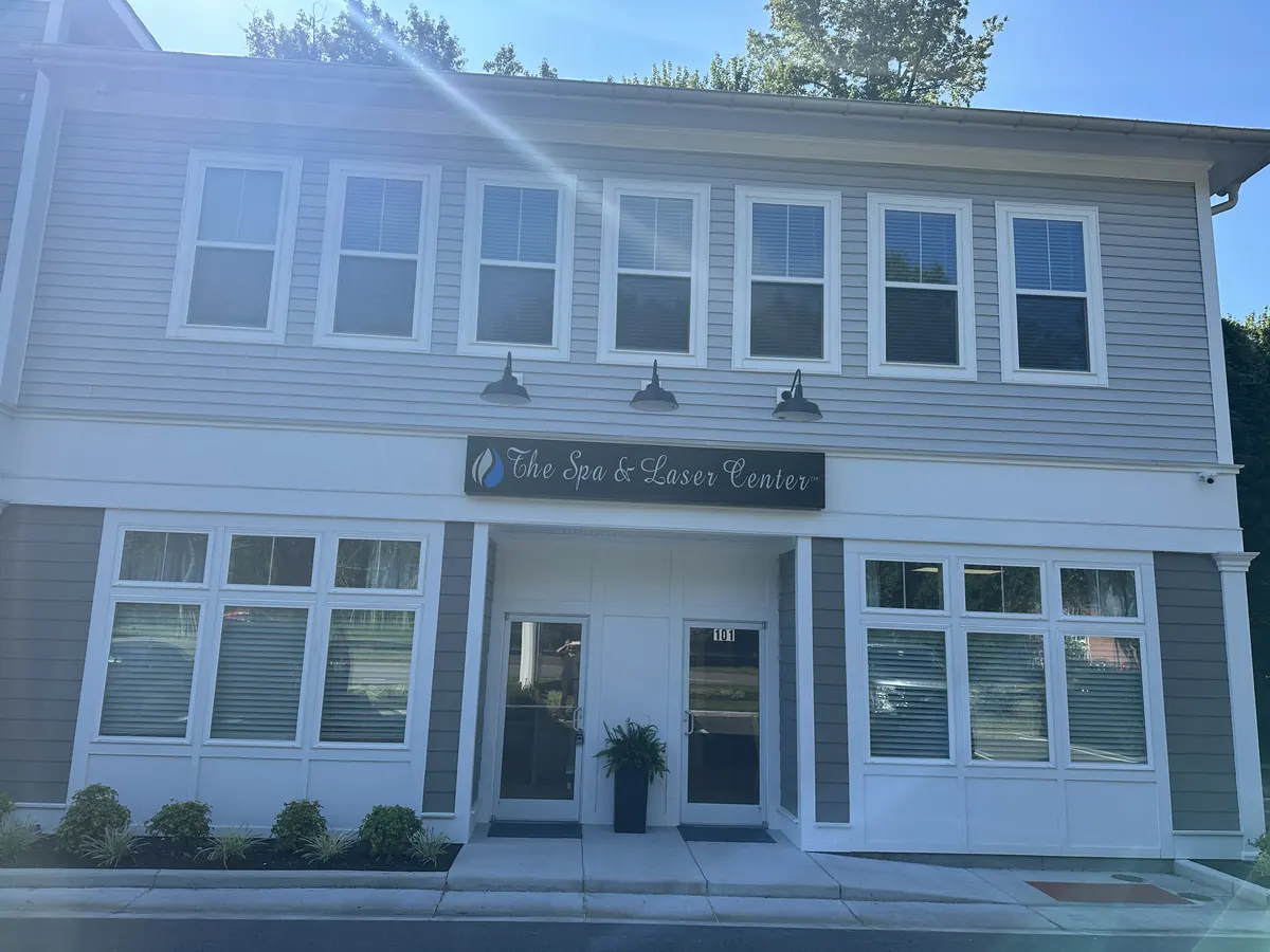 Two-story gray building with an illuminated sign above a white entrance and two glass doors